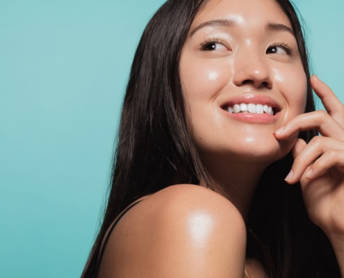 Close up of cute asian girl with glowing skin against blue background. Beautiful face of girl with fresh healthy skin.